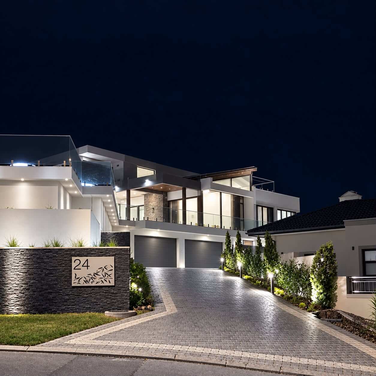 A modern home at night with wall lights, downlights and garden uplighting switched on