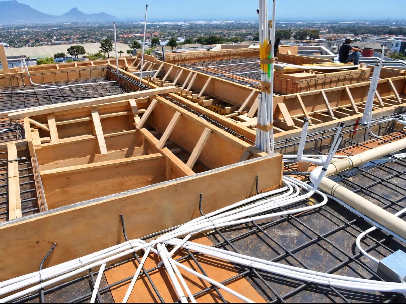 Electrical conduit laid across slab formwork on a building site, with Table Mountain in the distance