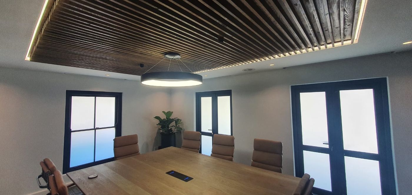 A boardroom with a ring pendant and strip lighting around a slatted timber ceiling